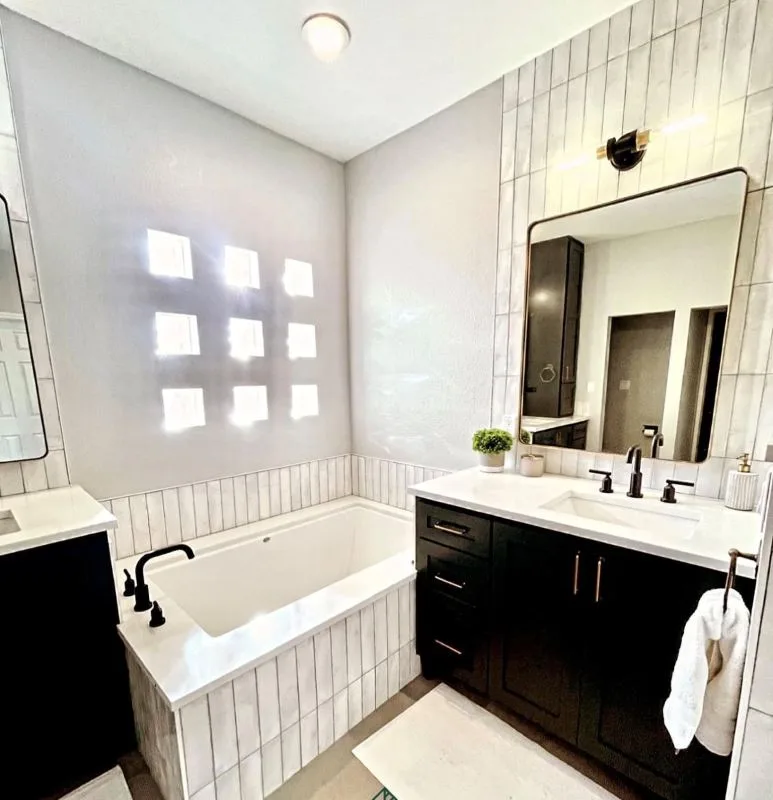 Completed bathroom with a bath, dark vanity and white tiling