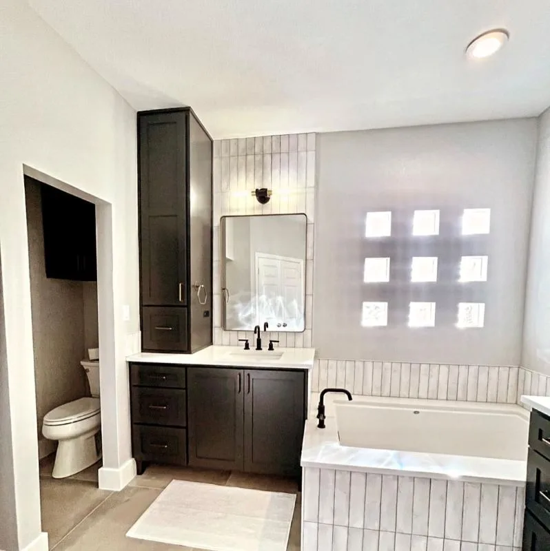 Completed bathroom with a dark vanity, bath and tiled walls