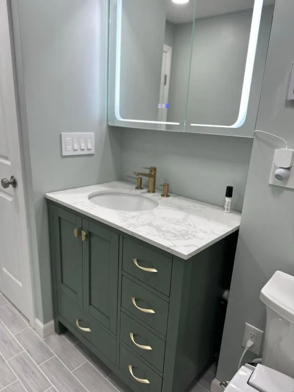 Completed vanity in green cabinetry with brass tapware and a stone top