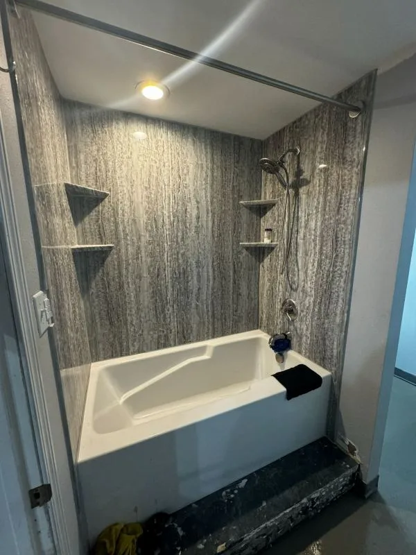 Completed bath with a grey marble tiled surround and shelves